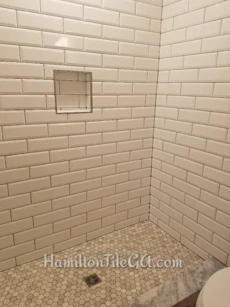This one is a beveled tile shower. A very bold look. We have hex wood look tile on the floor with a hard surface curb matching the top on the vanity. This is a 12x12 soap niche edged with Quadec brushed nickle profiles. Tile purchased at Traditions …